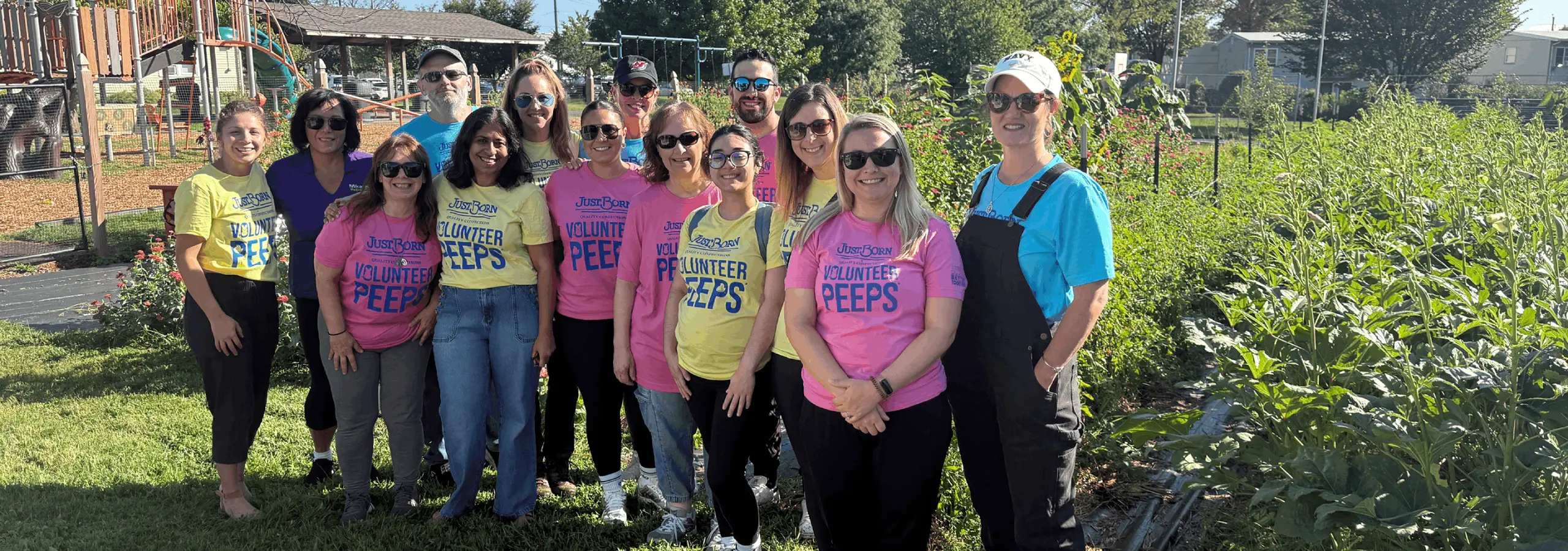 A group of smiling volunteers wearing colorful shirts pose together in an outdoor garden setting.