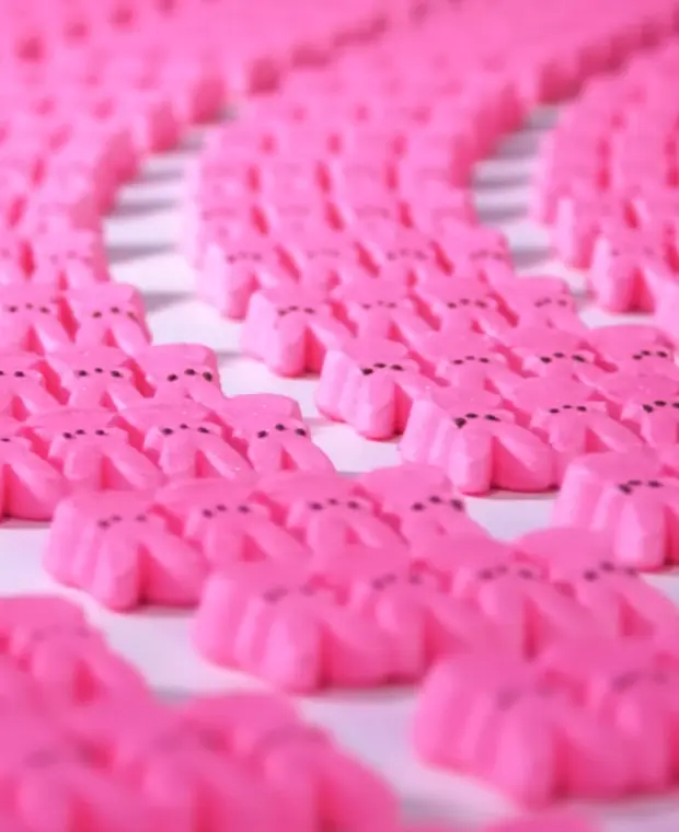 Numerous pink marshmallow Peeps bunnies arranged in curving rows on a white surface.