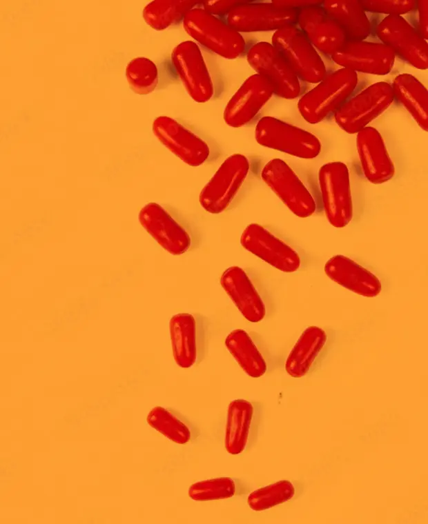 A scattered trail of small, bright red, oblong candies on a solid orange-yellow surface.